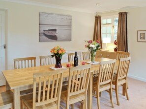 A dining room with a wooden table, six chairs, two vases with flowers, a bottle, and glasses.