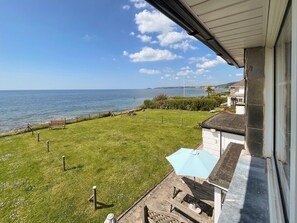 A balcony with a view of the sea, a grassy lawn, and a white building with a stone facade. - Former coastguard cottage with spectacular view from Rame Head to Looe Island. (Downderry, near Looe)