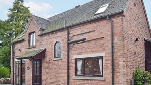 A brick building with a pitched roof, a large arched window, and a door with a metal handle.