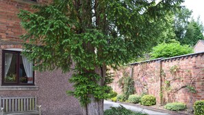 A brick building with a large tree in front, a bench, and a flower bed.