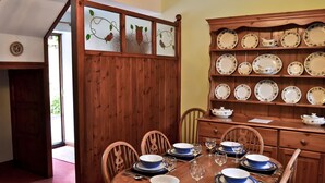 A dining room with a wooden table set for six, surrounded by chairs. A wooden cabinet with plates and a pitcher is to the right.