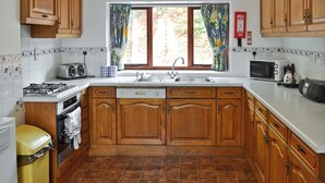 A kitchen with wooden cabinets, a sink, a stove, a microwave, and a window with curtains.