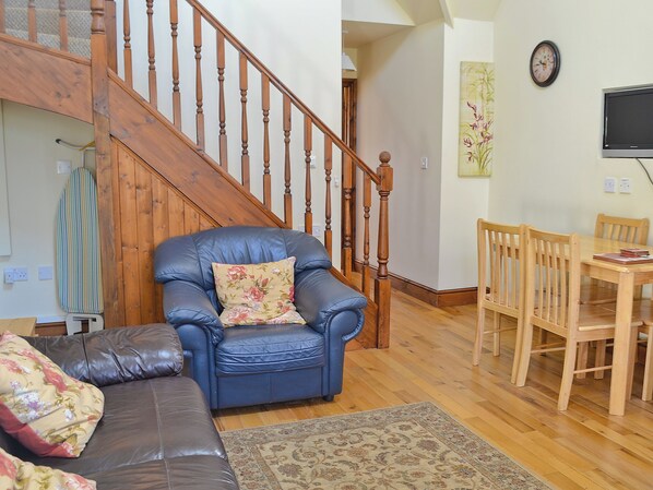 A living room with a blue leather armchair, a wooden dining table with chairs, a staircase, and a painting on the wall. - Rose Cottage - 30502 (Beddingham, near Lewes)