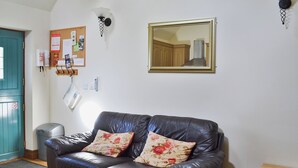 En stue med en mørk lædersofa, blomstrede puder, et træskab, en vægmonteret lampe og et indrammet spejl.