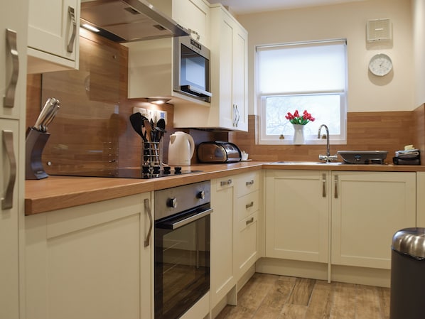 A modern kitchen with white cabinets, a built-in oven, a microwave, and a window with a view of the outside. - 1 bedroom accommodation in Keswick (Keswick)