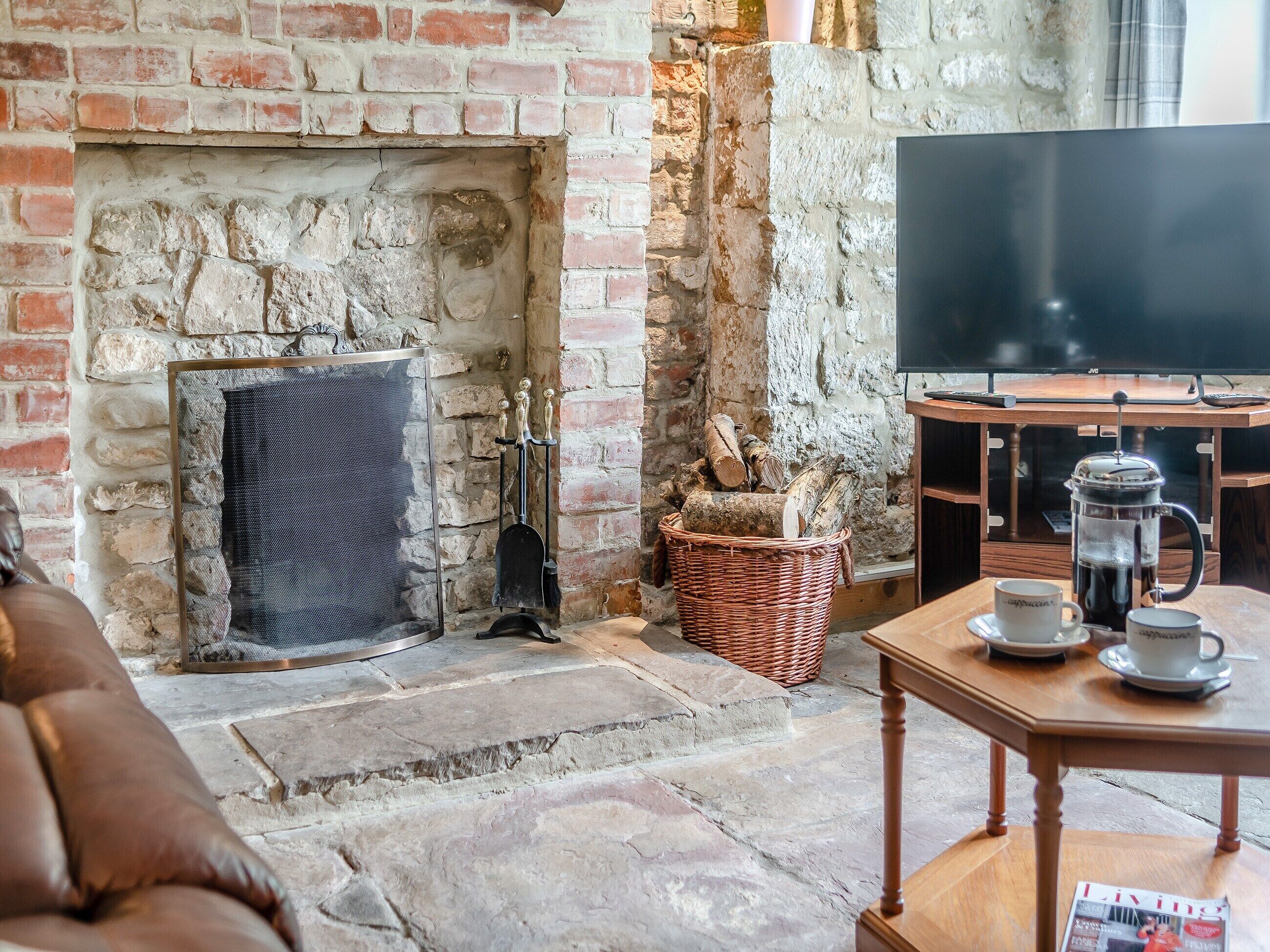 A cozy living room with a stone fireplace, a television, and a coffee table with cups and a magazine.