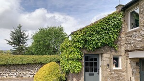 Ein Steinhaus mit einer grauen Tür, einem kleinen Fenster mit einer Blume und einer Statue einer Person.