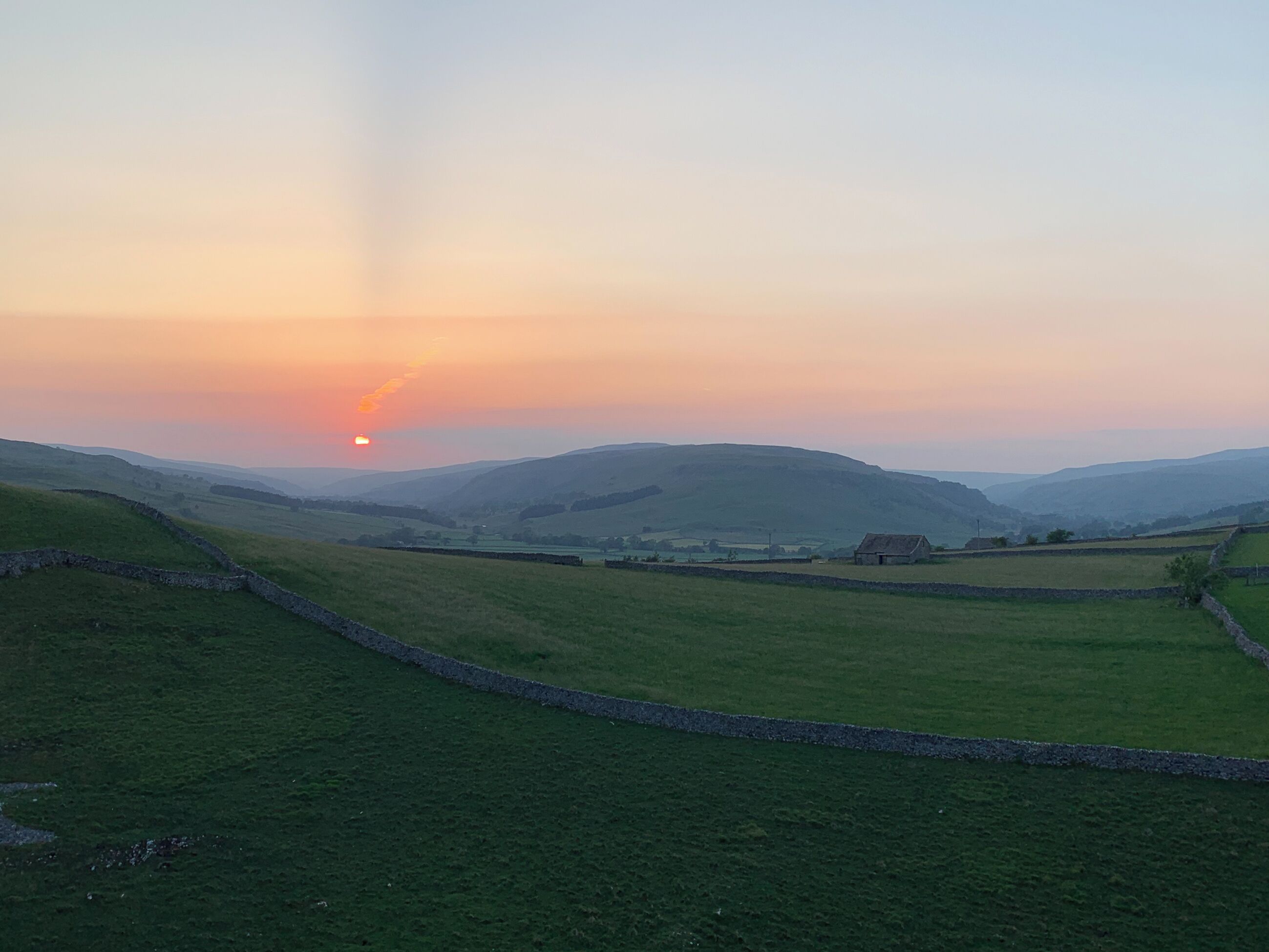 A rural landscape with rolling hills, stone walls, and a small building in the distance.
