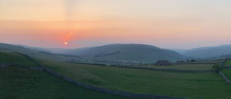 A rural landscape with rolling hills, stone walls, and a small building in the distance.