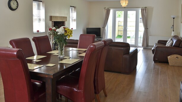 A dining area with a table set for four, surrounded by red chairs. There is a vase with flowers on the table, and a television is visible in the background. - 4 bedroom accommodation in Longhirst, near Morpeth (Longhirst, near Morpeth)
