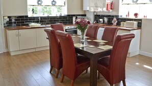 A modern kitchen with a dining area. It includes a wooden table with chairs, a vase with flowers, and a refrigerator. - 4 bedroom accommodation in Longhirst, near Morpeth (Longhirst, near Morpeth)