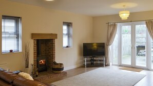 A living room with a fireplace, a TV on a stand, a sofa, and a large window with curtains. - 4 bedroom accommodation in Longhirst, near Morpeth (Longhirst, near Morpeth)