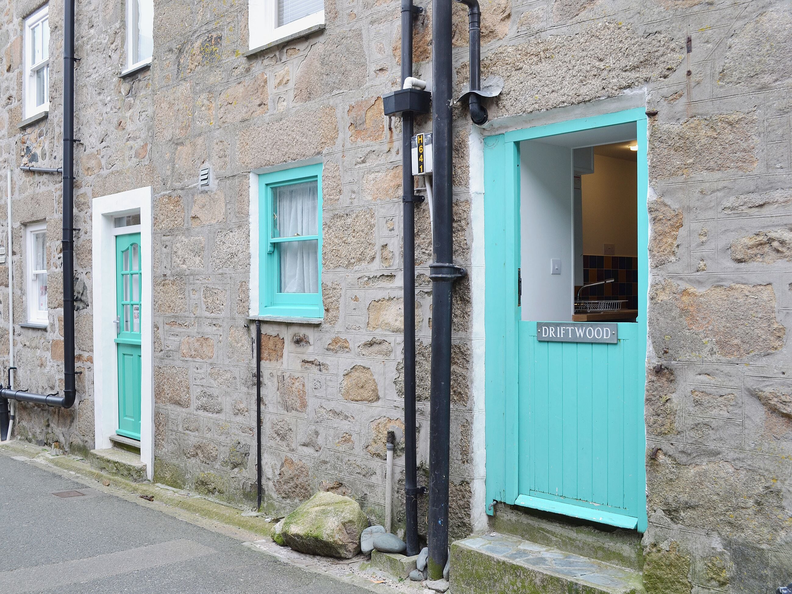 A stone building with turquoise doors and windows, a visible sign reading 'DRIFTWOOD,' and a small step leading to the entrance.