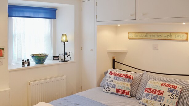 A bedroom with a bed, a window with curtains, a bedside lamp, and a wall sign. - 1 bedroom accommodation in St Ives (St Ives)