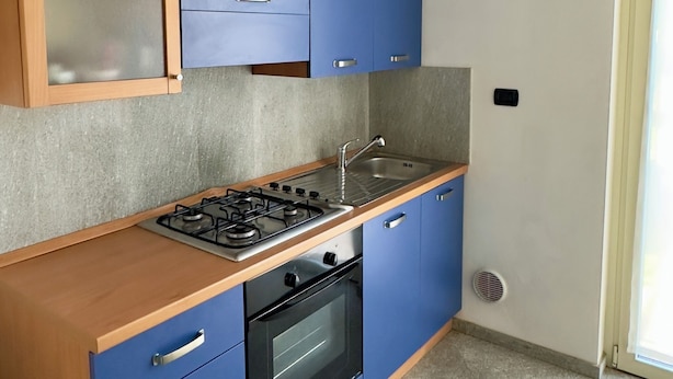 A compact kitchen with blue cabinets, a gas stove, a sink, and a built-in oven.