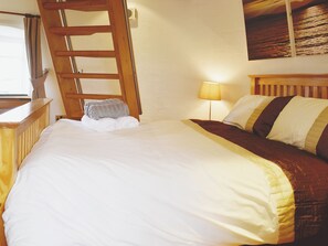 Un lit bien fait, avec une tête de lit en bois, une lampe de chevet et une serviette sur le sol.