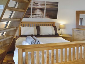 Un lit en bois avec une tête de lit, une table de chevet avec une lampe, une commode en bois et une vue sur la mer par la fenêtre.