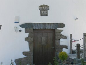 Un bâtiment doté d’une arche en pierre et d’une porte en bois, une enseigne au-dessus de la porte indiquant « OIAFM 1833 », et une petite lampe sur le côté gauche.