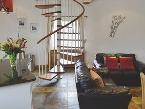 Un salon avec un escalier en colimaçon, un canapé en cuir noir agrémenté de coussins rouges et un vase de fleurs posé sur le comptoir.