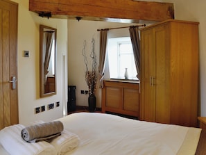 A bedroom with a large bed, wooden wardrobe, a mirror, and a window with curtains. - 2 bedroom accommodation in Tynlon, near Rhosneigr (Tynlon, near Rhosneigr)