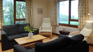 A living room with a black sofa, a white armchair, a wooden coffee table, and a vase with green plants. - 3 bedroom accommodation in Turriff (Turriff)