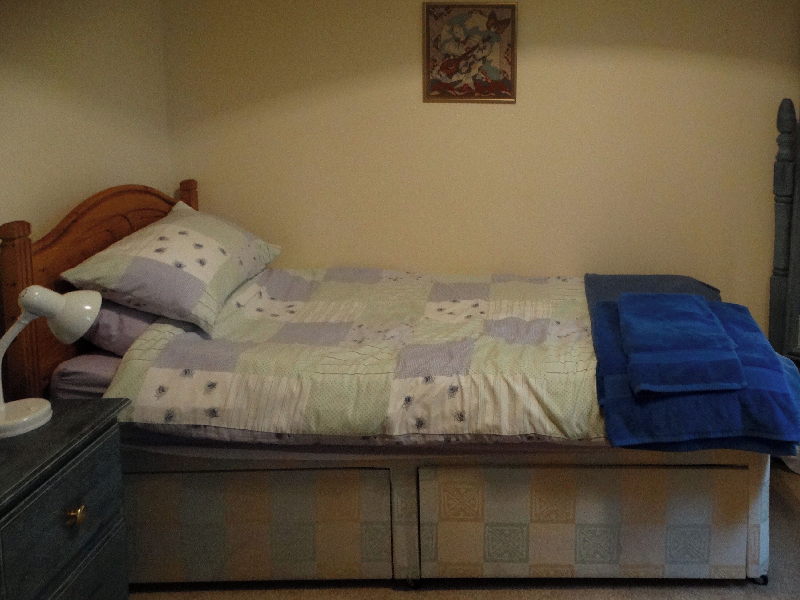 Un letto singolo con testiera in legno, una coperta, una trapunta blu e una lampada da comodino.