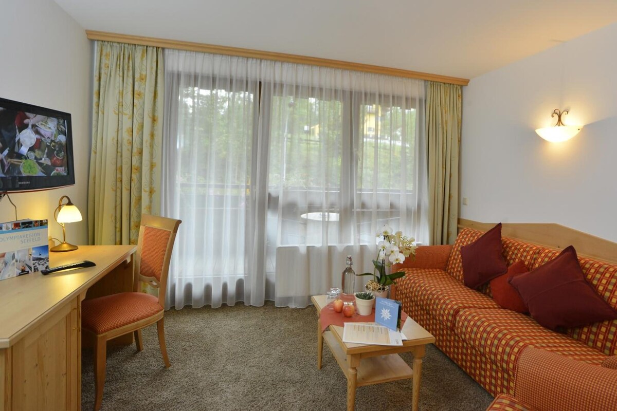 Una habitación acogedora con sofá, escritorio con lámpara, televisión y ventana con cortinas.