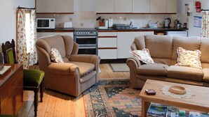 A compact living space with a kitchenette, two sofas, a wooden coffee table, and a patterned rug. - 3 bedroom accommodation in John O’ Groats (John O’ Groats)