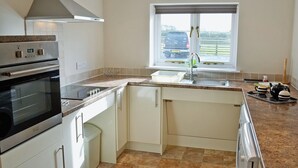 A modern kitchen with a built-in oven, a stainless steel range hood, a window with a view of the outside, and a countertop with a kettle and teapot. - 2 bedroom accommodation in Towan Cross, near Porthowan (Towan Cross, near Porthowan)