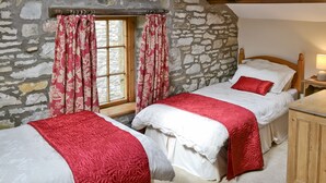 Une chambre avec deux lits, des murs en pierre, une lucarne et une table de chevet en bois avec une lampe.