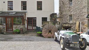 Une voiture ancienne est garée devant un bâtiment dont la façade est en pierre et l’extérieur est peint en blanc.