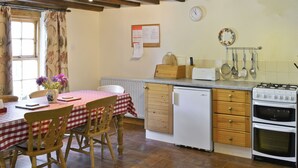 Une cuisine avec une table en bois, des chaises, un réfrigérateur, une cuisinière et une horloge au mur.