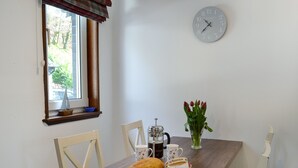 Un tavolo da pranzo con una pagnotta, grappe, un coltello, una caffettiera, una tazza e un vaso con fiori.