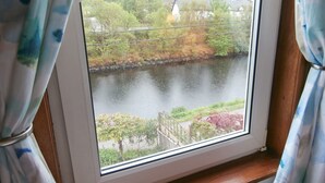 Una finestra con vista su un fiume, vegetazione e un edificio in lontananza.