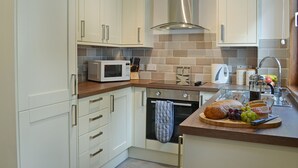 Una cucina moderna con mobili bianchi, una cappa aspirante in acciaio inox, un forno a microonde e un piano di lavoro in legno con una pagnotta e grappoli d'uva.