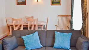 Un salón con un sofá gris, dos cojines azules, una mesa de comedor de madera con sillas y dos cuadros en la pared.