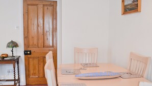 Un comedor con puerta de madera, una mesa con individuales, sillas y una lámpara en una mesita auxiliar.