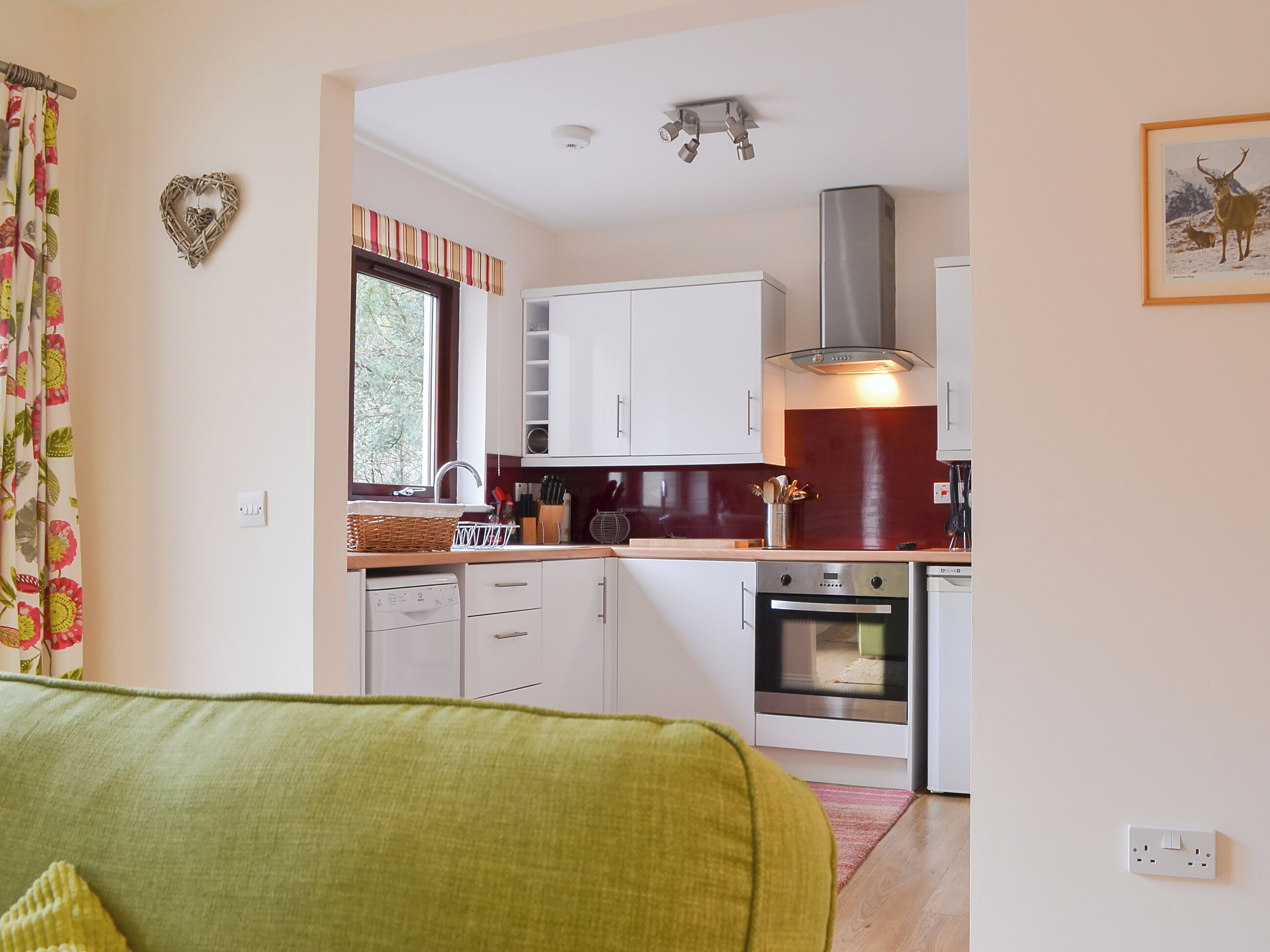 A modern kitchen with white cabinets, a stainless steel range hood, and a window with curtains.