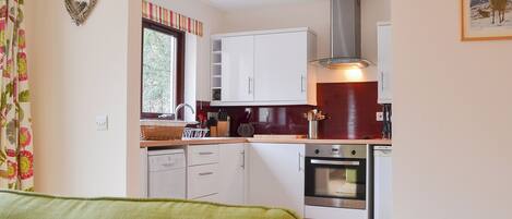 A modern kitchen with white cabinets, a stainless steel range hood, and a window with curtains.