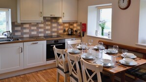 Een moderne keuken met witte kasten, een betegelde spatwand en een eethoek voor vier personen, met witte stoelen en een houten tafel.