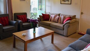 Een gezellige woonkamer met een houten salontafel, twee fauteuils, een bank en een deur naar een tuin.