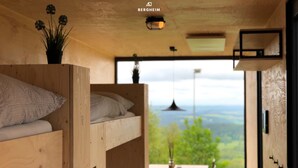 A cozy cabin interior with a bunk bed, a dining area with a table and chairs, and a large window offering a scenic view. - BERGHEIM Container Lofts, Holidays directly in the Ski & Bikewelt, Container "Drop" (Schöneck/Vogtland)