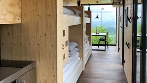 A narrow wooden interior with bunk beds, a kitchen area, and a dining table with a view. - BERGHEIM Container Lofts, Holidays directly in the Ski & Bikewelt, Container "Drop" (Schöneck/Vogtland)