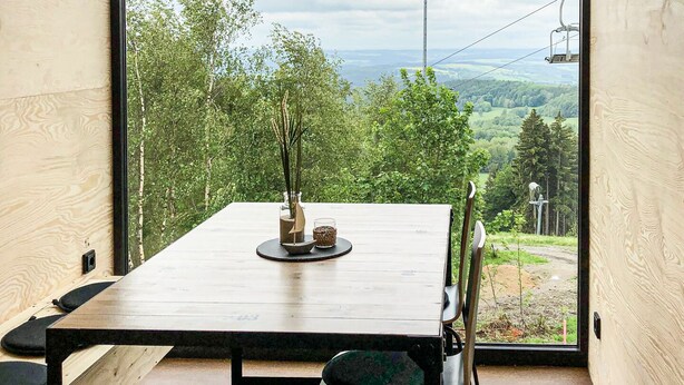 A modern interior with a large window offering a view of a forest and distant hills. - BERGHEIM Container Lofts, Holidays directly in the Ski & Bikewelt, Container "Drop" (Schöneck/Vogtland)