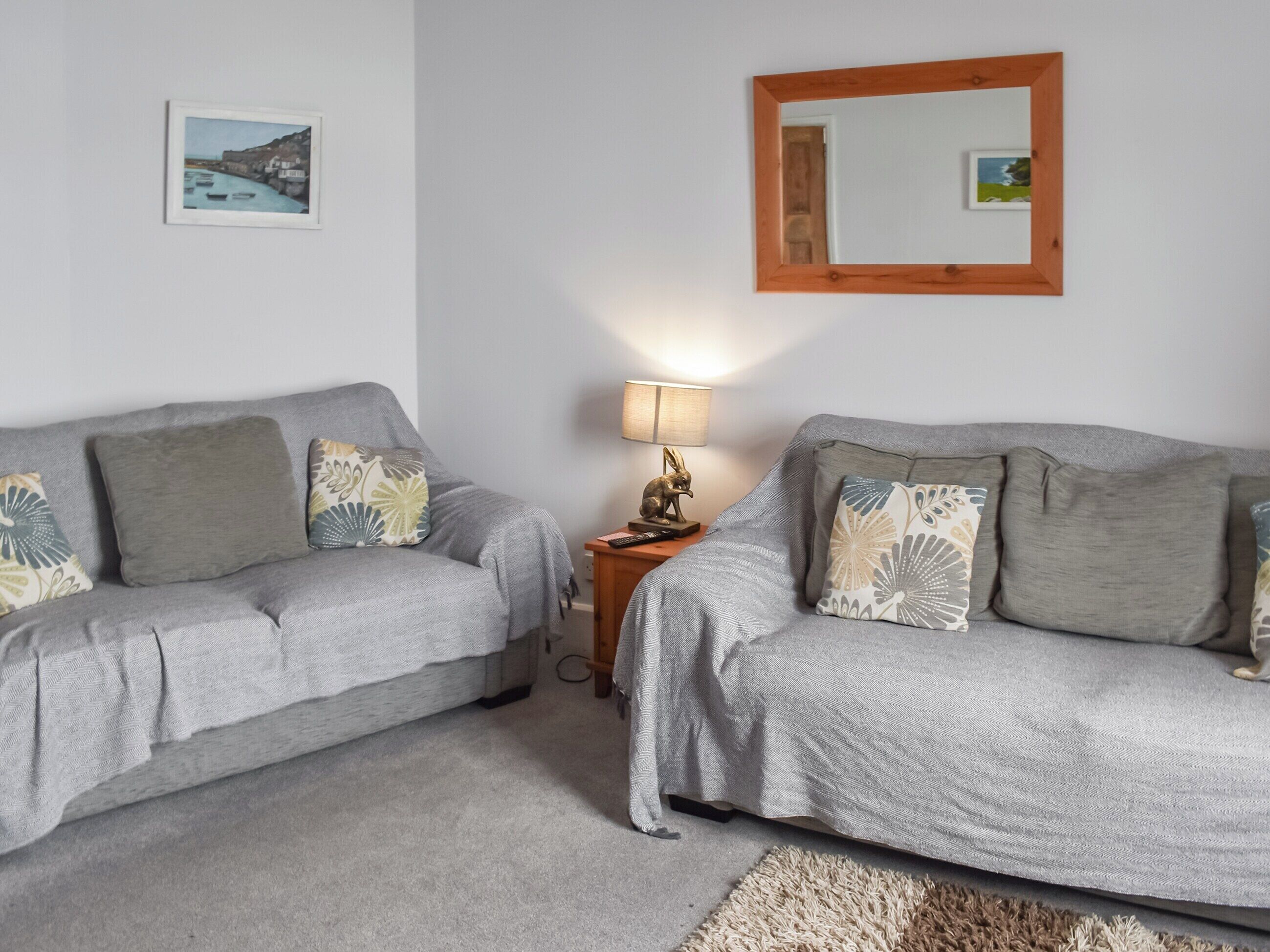 A room with two grey sofas, a small wooden side table with a lamp, and a mirror on the wall.