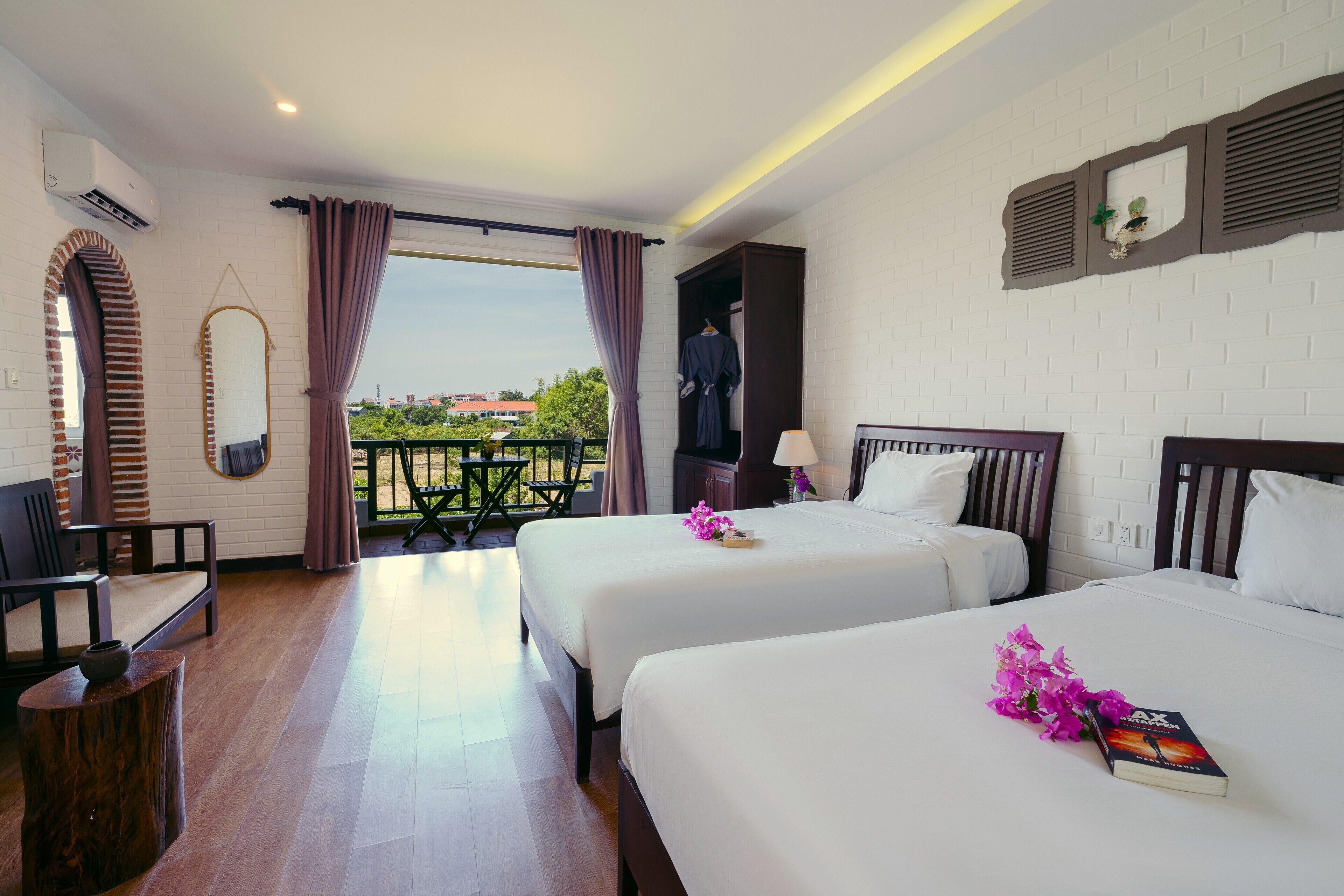 A hotel room with two beds, a sitting area with a chair and table, a large mirror, and a view of the outdoors.