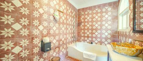 A bathroom with patterned tiles, a bathtub, a sink with a bowl basin, and a toilet.