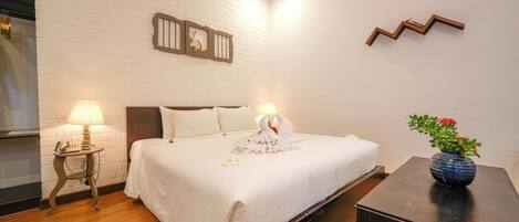 A neatly made bed with white bedding, a bedside lamp, a small table with a vase of flowers, and a wall-mounted air conditioner.