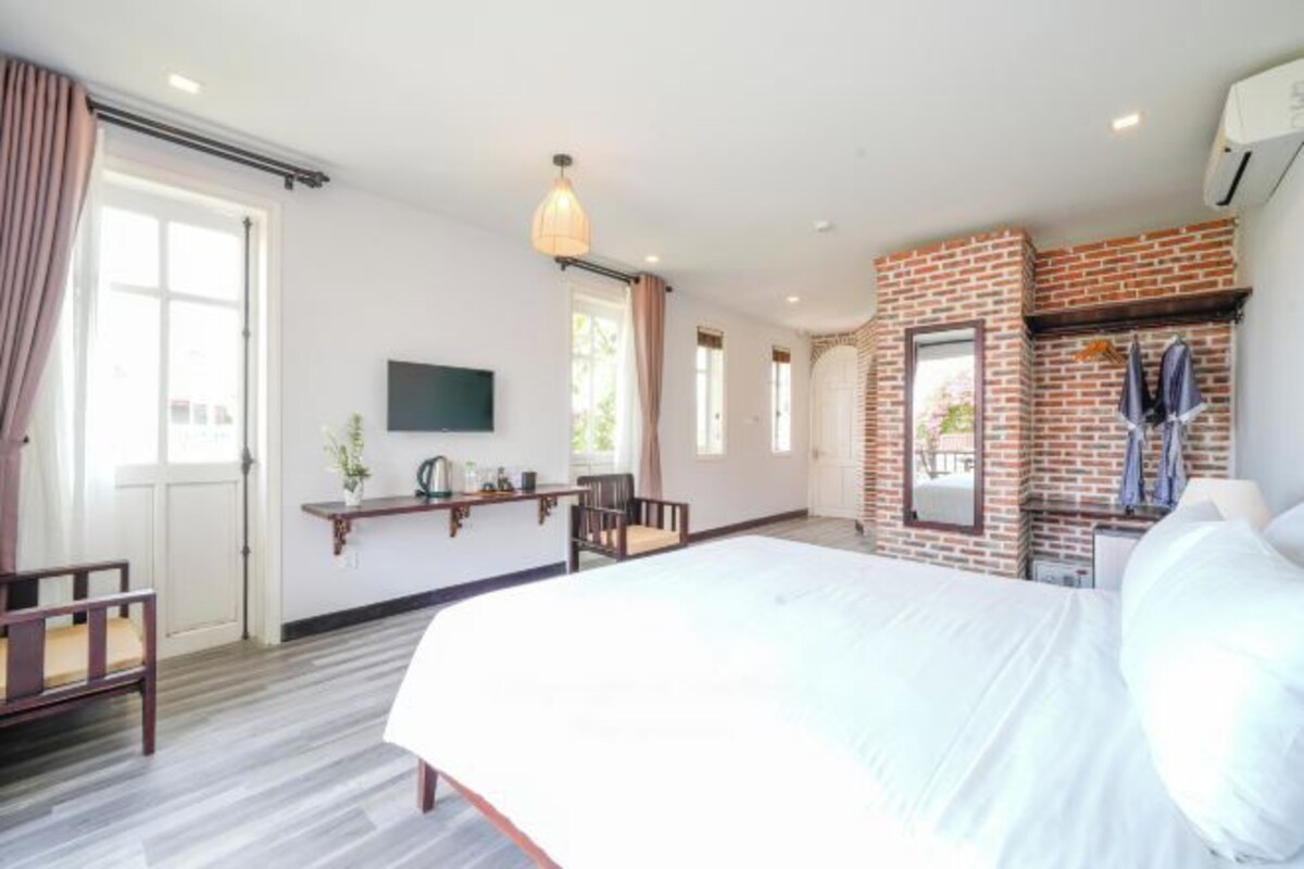 A hotel room with a large bed, a desk with a chair, a TV, and a brick accent wall.