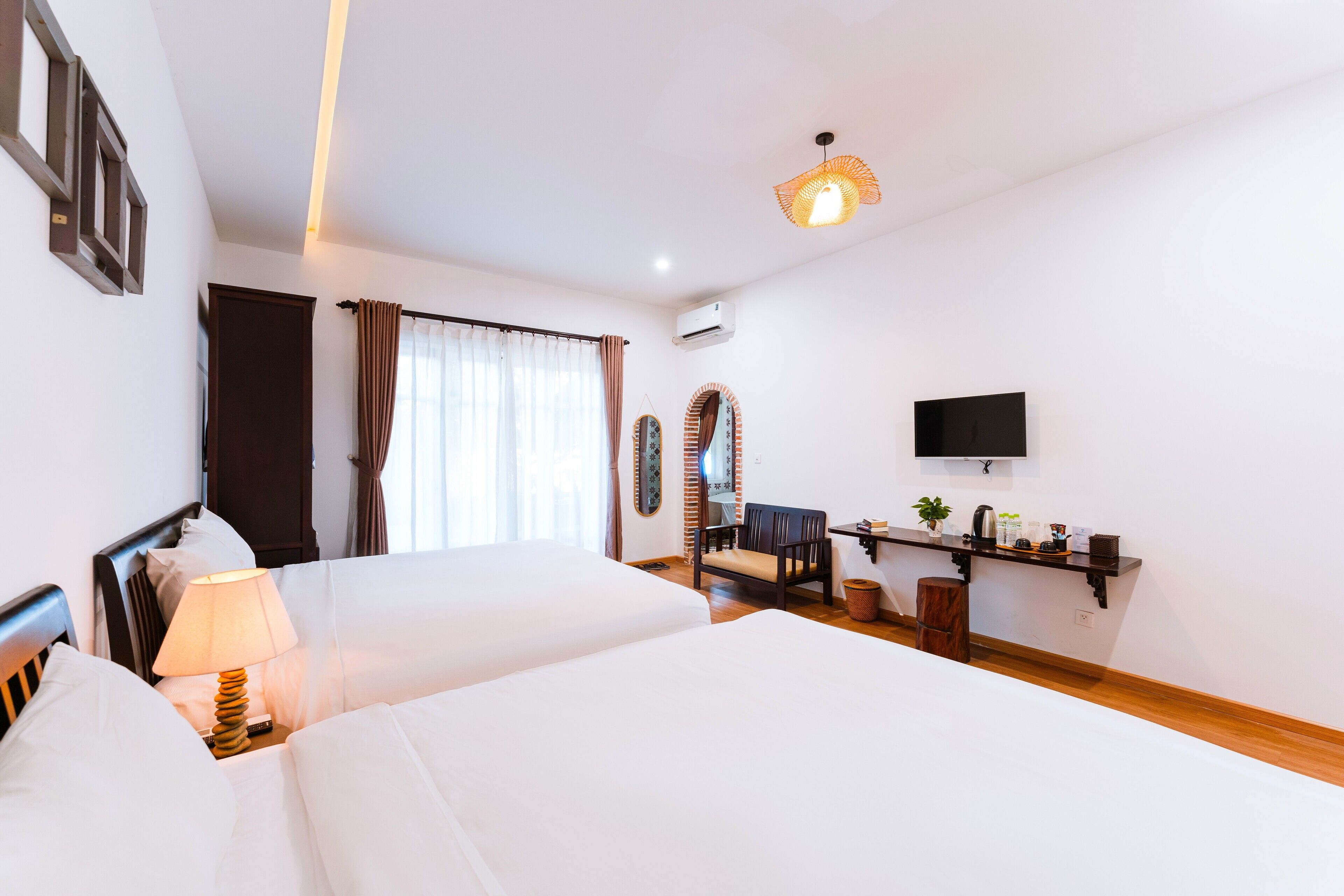 A hotel room with two beds, a desk with a chair, a TV, and a window with curtains.